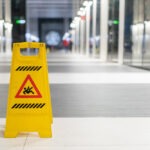 A yellow slippery floor sign sits in a building hallway.