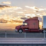 A red semi-truck drives against the sunset
