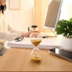 Hourglass beside smartphone and eyeglasses on desk surface