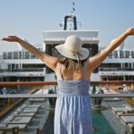 Woman in sunhat with raised arms overlooking cruise ship deck and pool