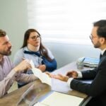 Man holding document while speaking with suited attorney across office desk