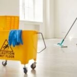 janitor mopping floor beside caution wet floor sign and mop bucket