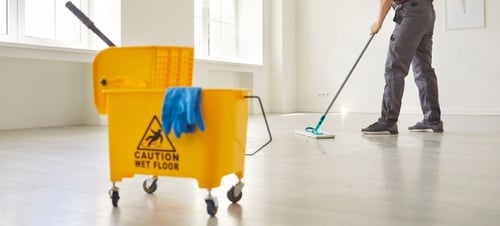 janitor mopping floor beside caution wet floor sign and mop bucket