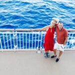 married couple standing on cruise ship deck railing with ocean below