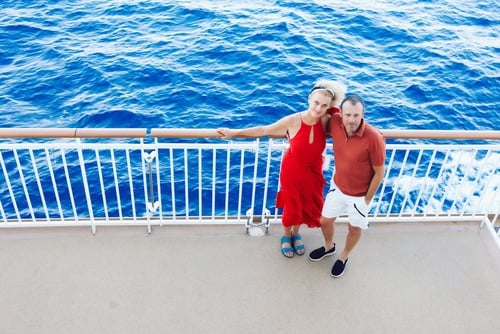 married couple standing on cruise ship deck railing with ocean below