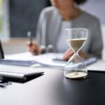 hourglass on office desk with professional reviewing documents in background