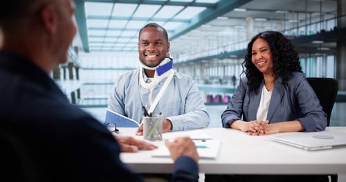 injured man wearing neck brace and arm sling meeting with legal professional