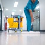 Cleaner in uniform mopping tiled floor with bucket and caution sign