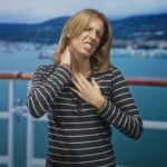 woman grimacing while clutching neck in pain on cruise ship deck