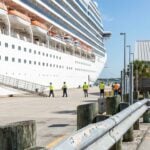 large cruise ship docked at port with workers in safety vests on pier