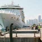 large cruise ship docked at port with workers in safety vests on pier