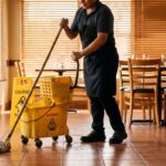 restaurant worker mopping tile floor beside caution wet floor mop bucket