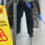 Caution Wet Floor sign with janitor mopping hallway floor in background