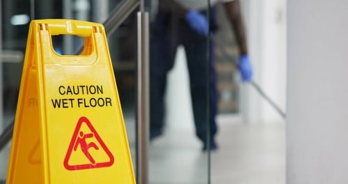 Caution Wet Floor sign with janitor mopping hallway floor in background