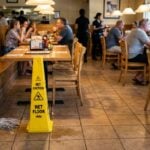 Wet Floor caution sign beside mop on restaurant tile floor with diners seated nearby