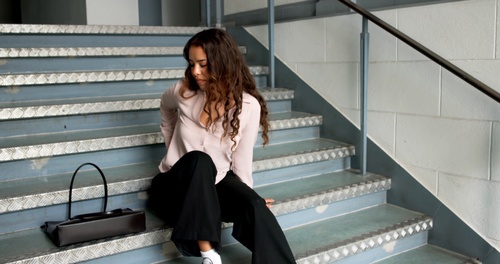 woman sitting on metal staircase steps with handbag beside her