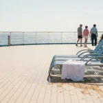 cruise ship deck with lounge chairs, towel, pool, and passengers near railing
