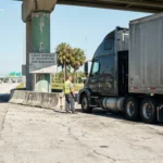 worker in safety vest inspecting semi-truck stopped under Florida highway overpass