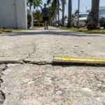 tape measure placed across cracked raised sidewalk with pedestrian approaching in background