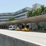Miami International Airport terminal exterior with taxis and shuttle van at curbside