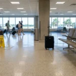 caution wet floor sign beside suitcase in airport terminal with travelers walking