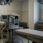 empty operating room with surgical table, overhead lights, and anesthesia monitor