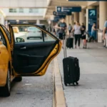 taxi with open door and suitcase on curb at busy airport terminal